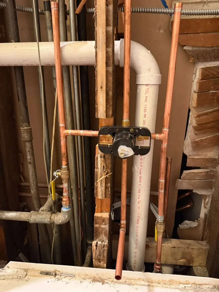 Shower valve rough-in with copper piping exposed near a brick chimney