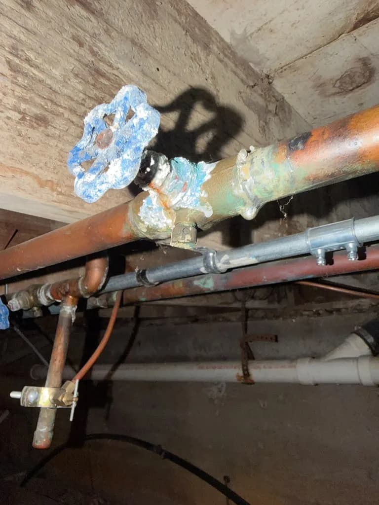 Corroded copper and galvanized pipes with an old shutoff valve in a basement ceiling