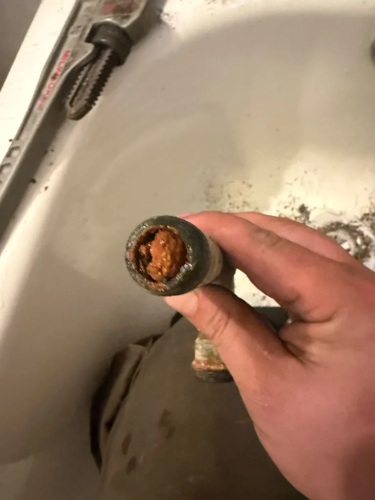 A hand holding a section of pipe with heavy rust and mineral buildup inside