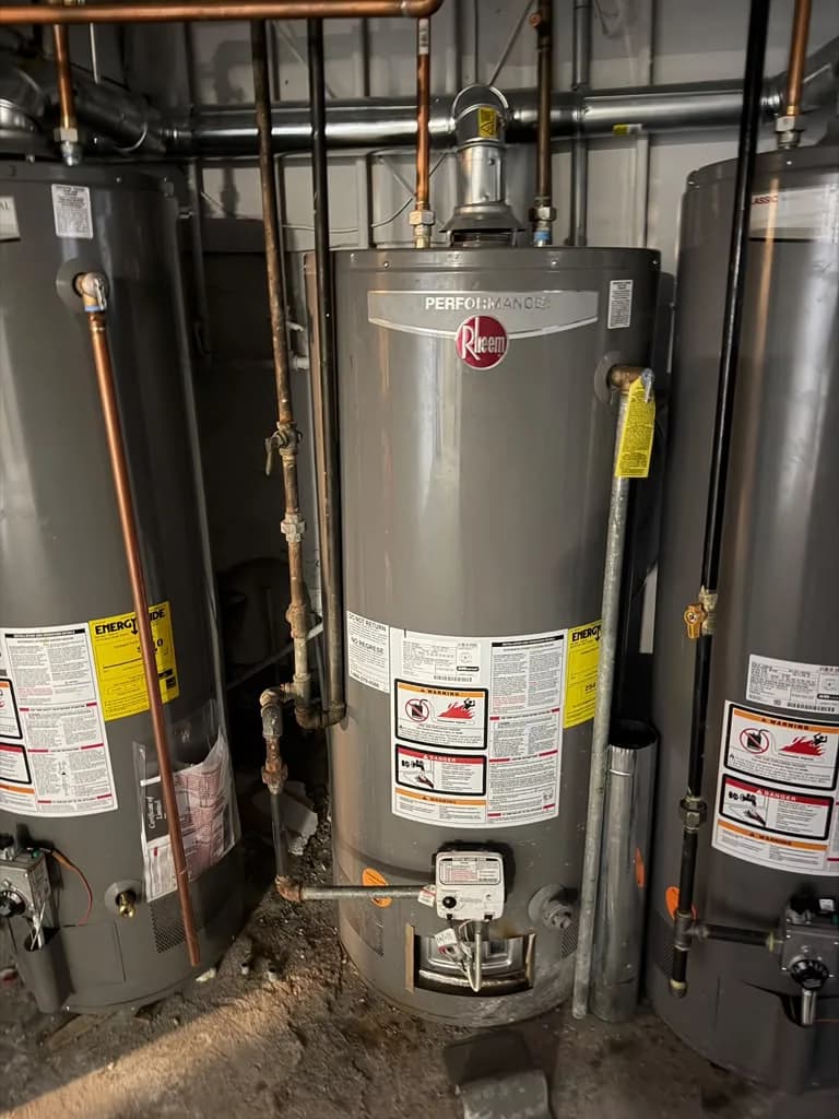 Three gas water heaters installed side by side in a mechanical room with copper piping overhead